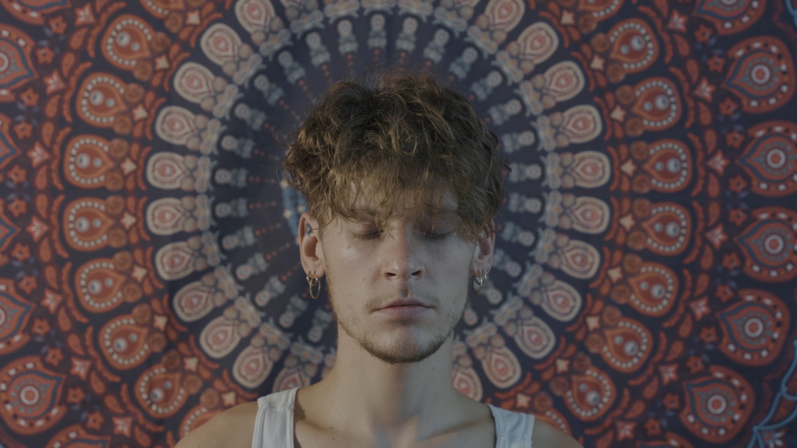 A person sitting in meditation in front of a mandala tapestry